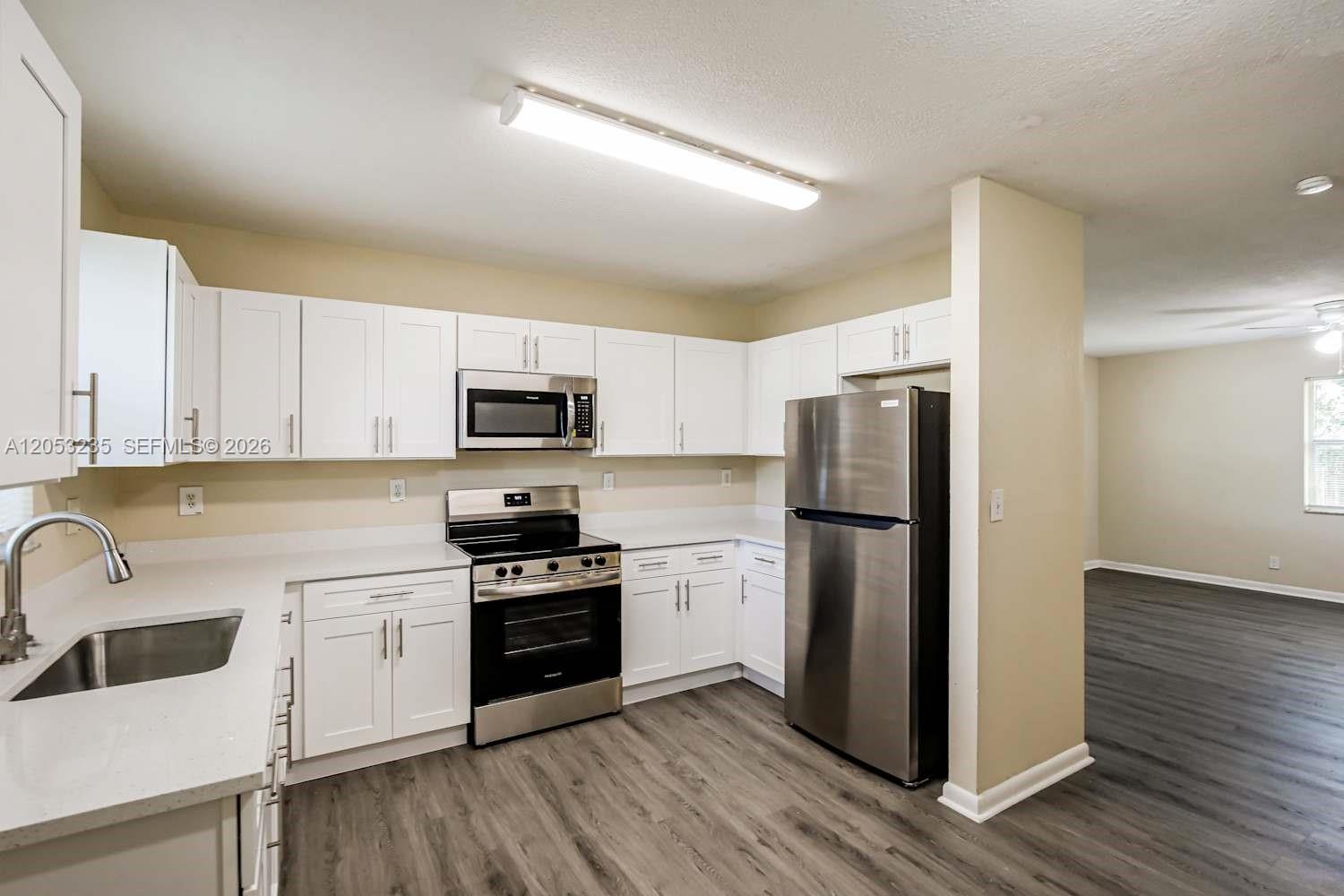 A kitchen features white cabinets, stainless steel appliances, and wood-look flooring — DAVIE, FL