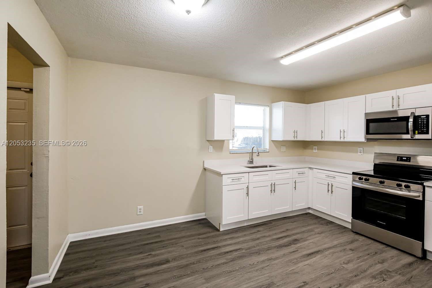 A kitchen features white cabinets, stainless steel appliances, and wood-look flooring — DAVIE, FL