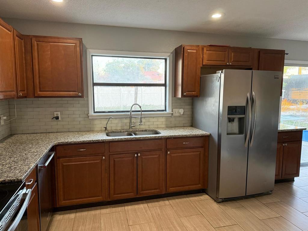 A kitchen features wood cabinets, granite countertops, a stainless steel refrigerator, and a subway tile backsplash — 1540 JUPITER AVENUE, DELTONA, FL