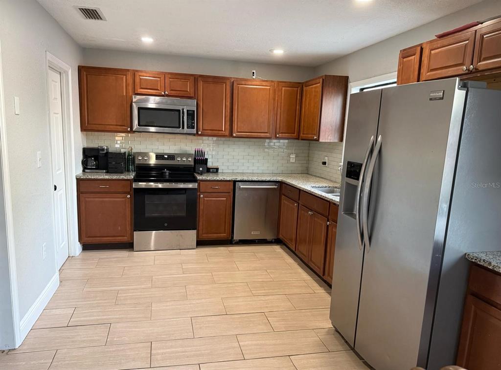 A kitchen with wood cabinets, stainless steel appliances, granite countertops, and light tile flooring — 1540 JUPITER AVENUE, DELTONA, FL