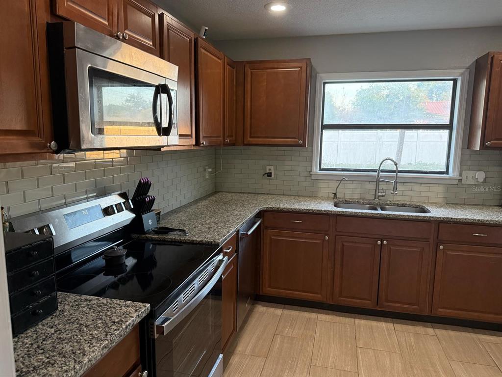 A kitchen features wood cabinets, granite countertops, a subway tile backsplash, and stainless steel appliances — 1540 JUPITER AVENUE, DELTONA, FL
