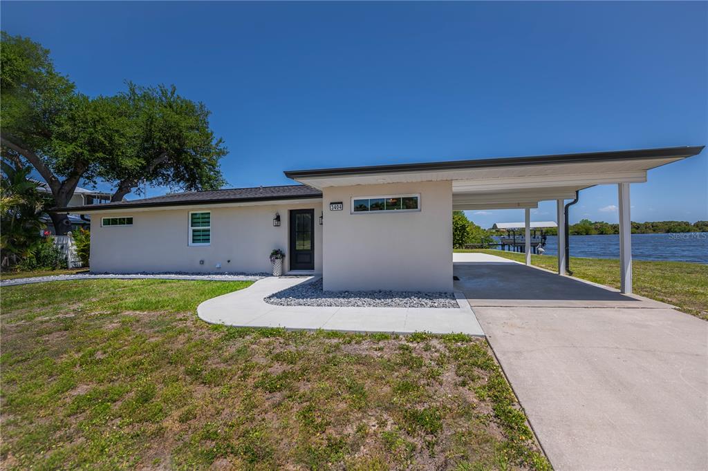 A single-story house with a carport sits along a waterfront property under a blue sky — 3404 LAKE VIEW BOULEVARD, PORT CHARLOTTE, FL