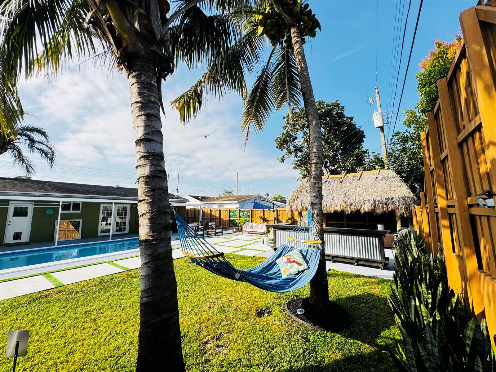 A backyard features a swimming pool, a blue hammock between palm trees, and a tiki bar — 7161 Sheridan Street, Hollywood FL 33024, HOLLYWOOD, FL