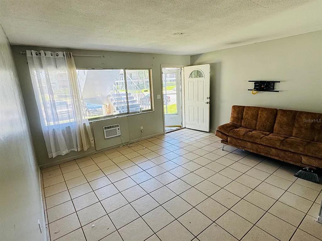 A living room with tile flooring, a brown sofa, a window, and an open door — 2353 SHELLEY STREET UNIT 11, CLEARWATER, FL