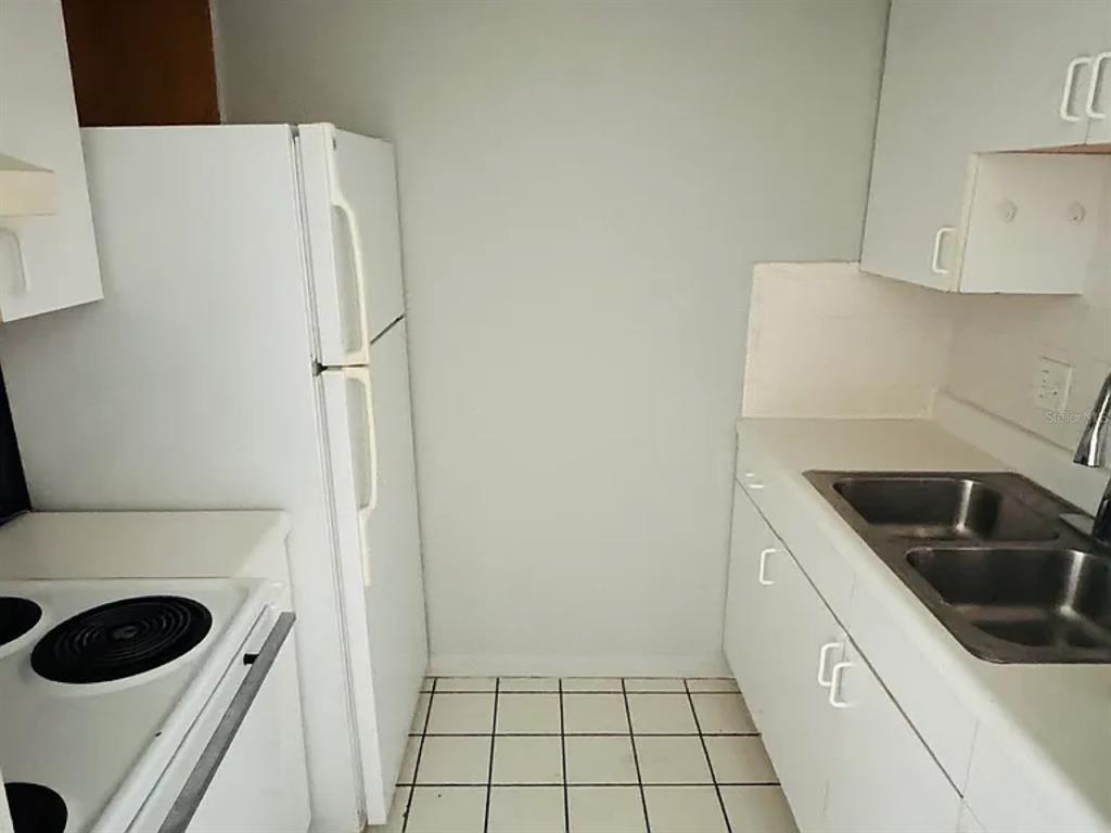 A small kitchen features white cabinets, a white refrigerator, a stove, and a double sink — 2353 SHELLEY STREET UNIT 11, CLEARWATER, FL