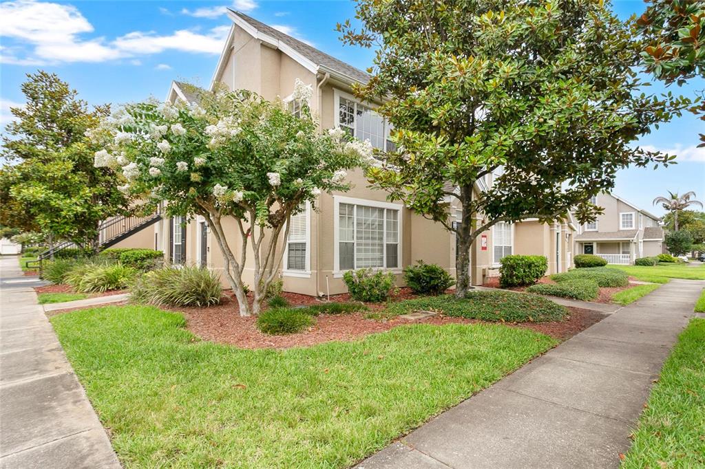 A beige two-story townhouse exterior features a white-flowering tree and a sidewalk in front — 8925 LEE VISTA BOULEVARD UNIT 2704, ORLANDO, FL