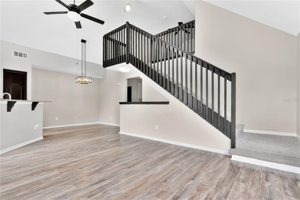An open living area features wood-look flooring, a staircase with black railings, and vaulted ceilings — 8925 LEE VISTA BOULEVARD UNIT 2704, ORLANDO, FL