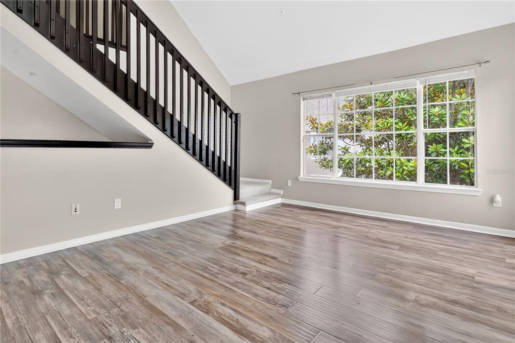 A living room features wood-look flooring, a black staircase railing, and a large window — 8925 LEE VISTA BOULEVARD UNIT 2704, ORLANDO, FL