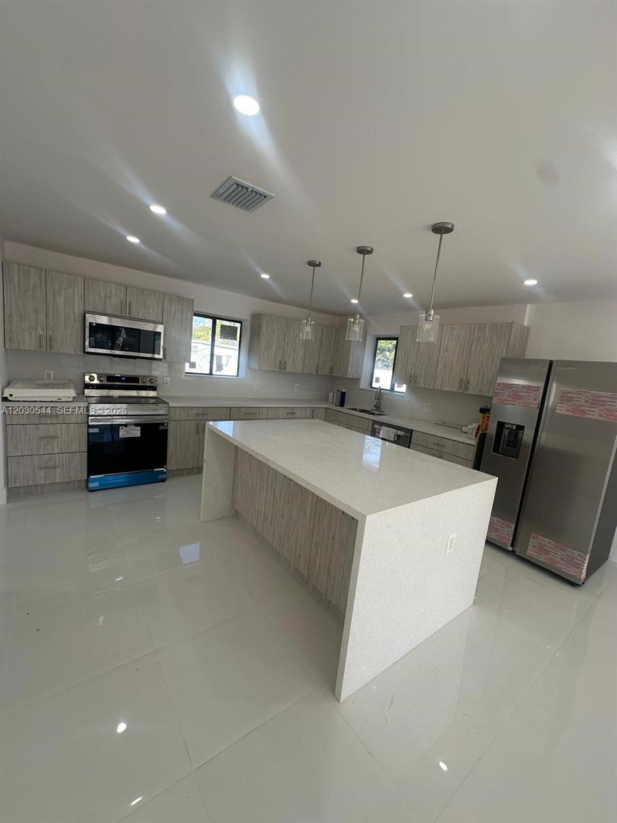 A modern kitchen features light wood cabinets, a large white island, and stainless steel appliances — 2041 NW 190th Ter, Miami Gardens FL 33056, MIAMI GARDENS, FL