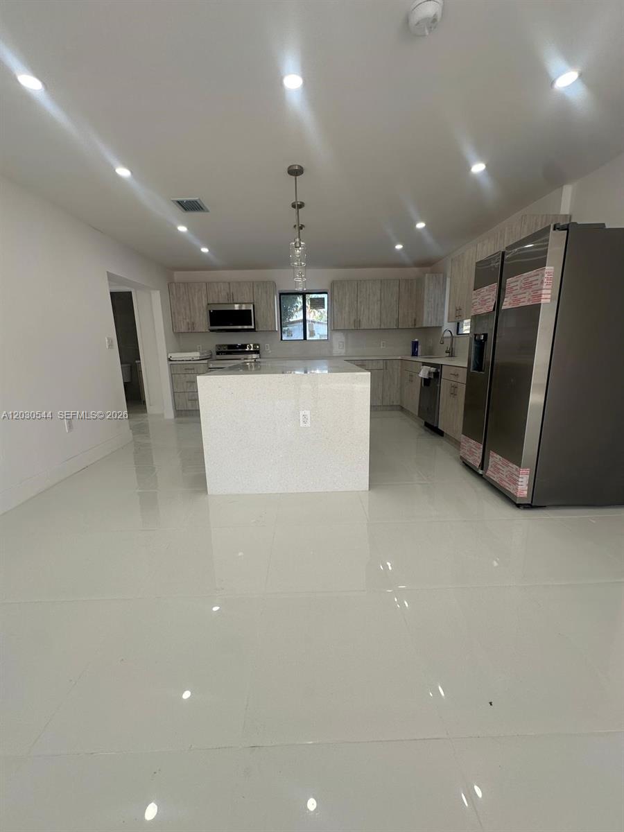 A modern kitchen features a central island, light-colored cabinetry, stainless steel appliances, and tile flooring — 2041 NW 190th Ter, Miami Gardens FL 33056, MIAMI GARDENS, FL