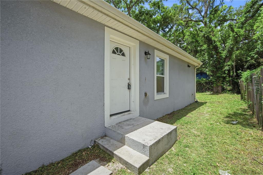 A gray stucco exterior wall features a white door with a lockbox and concrete steps — 8310 N BROOKS STREET, TAMPA, FL