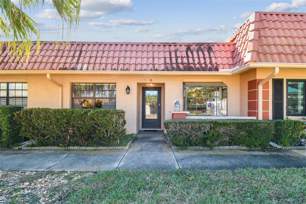 A single-story residential unit with a red tile roof, beige stucco walls, and a walkway — 19029 US HIGHWAY 19 N UNIT 10D, CLEARWATER, FL