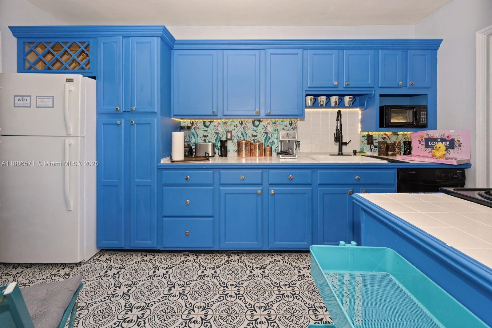 A kitchen features bright blue cabinets, patterned floor tiles, and a white tiled countertop — 1701 Fletcher St, Hollywood FL 33020, HOLLYWOOD, FL