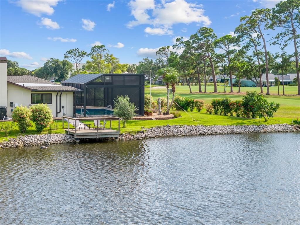 A house with a screened pool enclosure and wooden deck overlooking a pond and golf course — 3615 AVENIDA MADERA, BRADENTON, FL