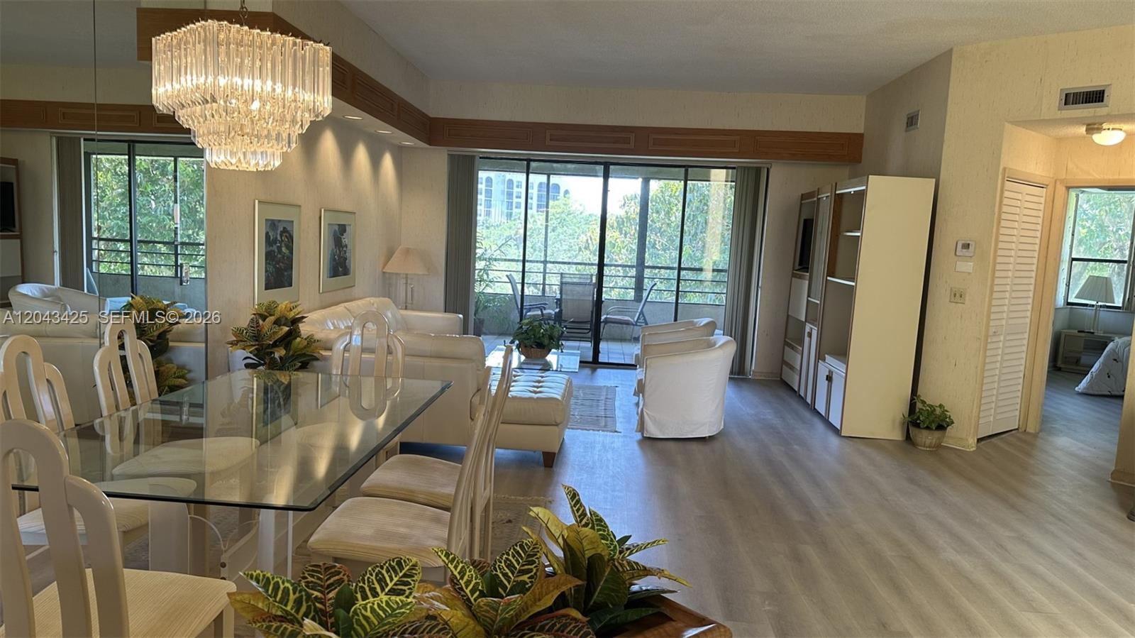 A living and dining area features a glass table, white furniture, and a crystal chandelier — 7472 La Paz Blvd # 301, Boca Raton FL 33433, BOCA RATON, FL