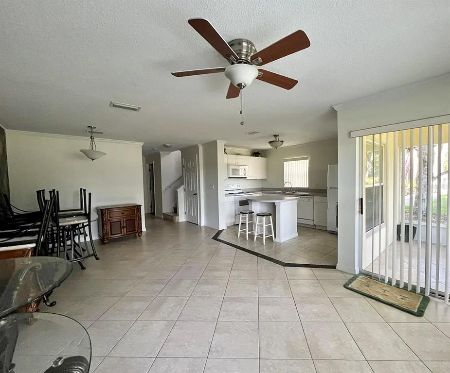 An open-concept living and dining area with tile floors leads to a kitchen with white cabinets — 2884 CLUB CORTILE CIRCLE, KISSIMMEE, FL