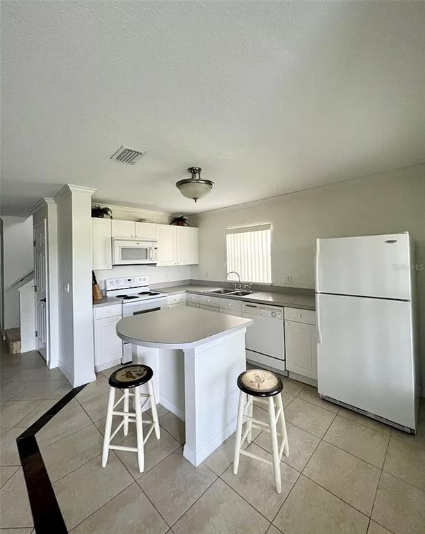 A kitchen features white cabinets, a central island with two stools, and white appliances — 2884 CLUB CORTILE CIRCLE, KISSIMMEE, FL