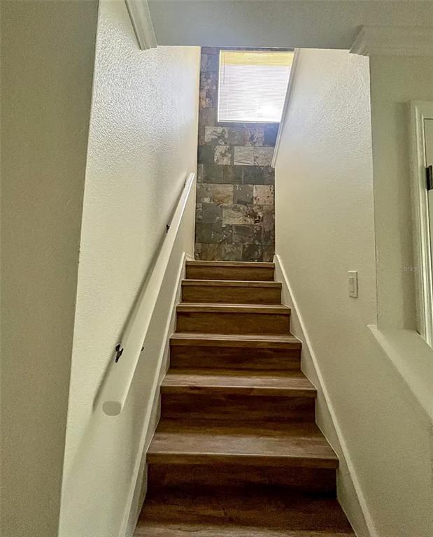 A staircase with wood-look steps and a white handrail leads to a stone-tiled accent wall — 2884 CLUB CORTILE CIRCLE, KISSIMMEE, FL