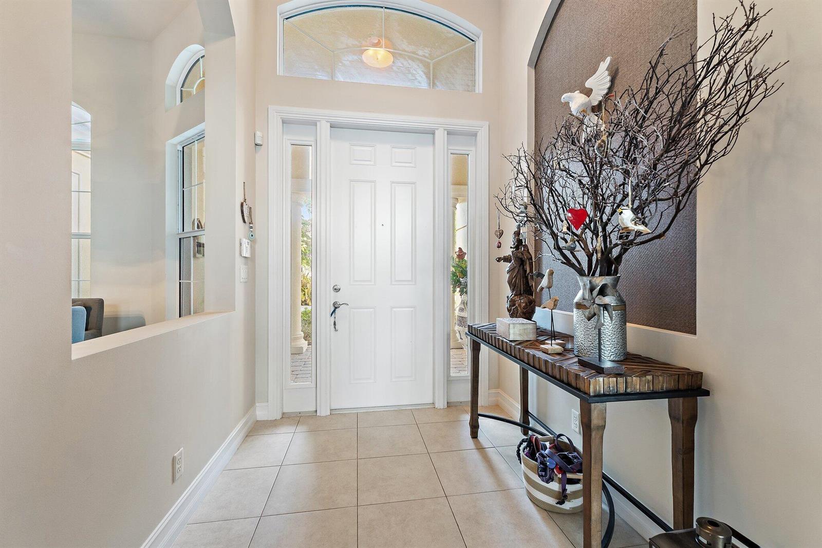 A bright entryway features a white front door, tile flooring, and a decorative console table — 114 Carmela Court, Jupiter FL 33478, JUPITER, FL