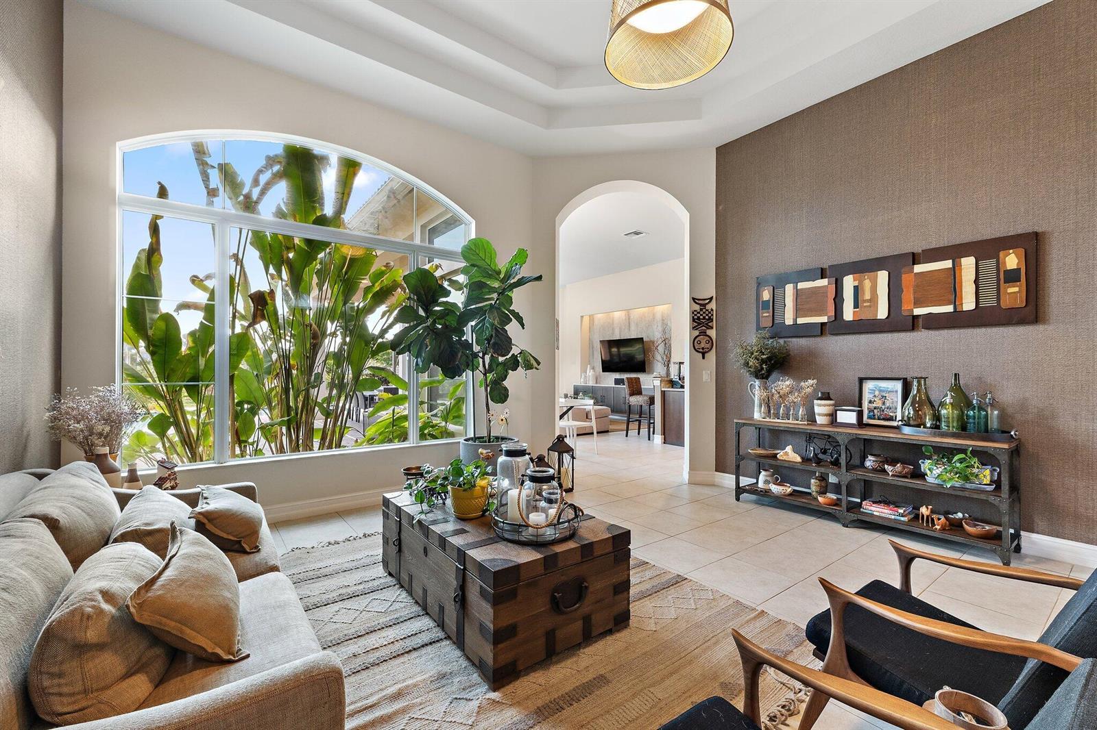 A living room features a large arched window, a trunk coffee table, and textured wallpaper — 114 Carmela Court, Jupiter FL 33478, JUPITER, FL