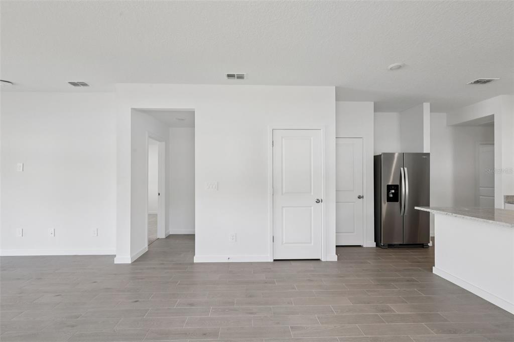 A bright, open-concept room features white walls, gray tile flooring, and a stainless steel refrigerator — 106 WANDERING CREEK WAY, PALM COAST, FL
