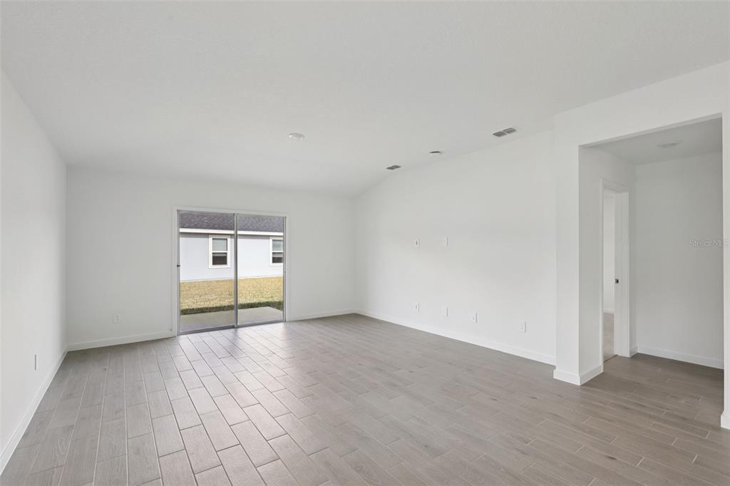 An empty living room features white walls, light wood-look tile flooring, and a sliding glass door — 106 WANDERING CREEK WAY, PALM COAST, FL
