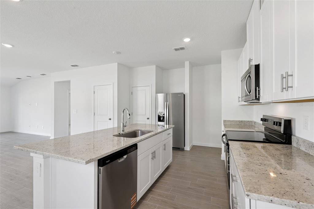 A modern kitchen features white cabinets, granite countertops, stainless steel appliances, and light wood flooring — 106 WANDERING CREEK WAY, PALM COAST, FL