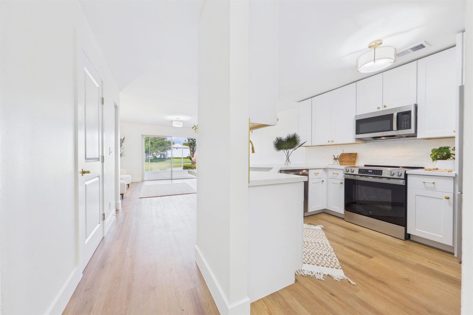 A bright kitchen with white cabinets and stainless steel appliances opens to a living area — 262 Timberwalk Trail, Jupiter FL 33458, JUPITER, FL