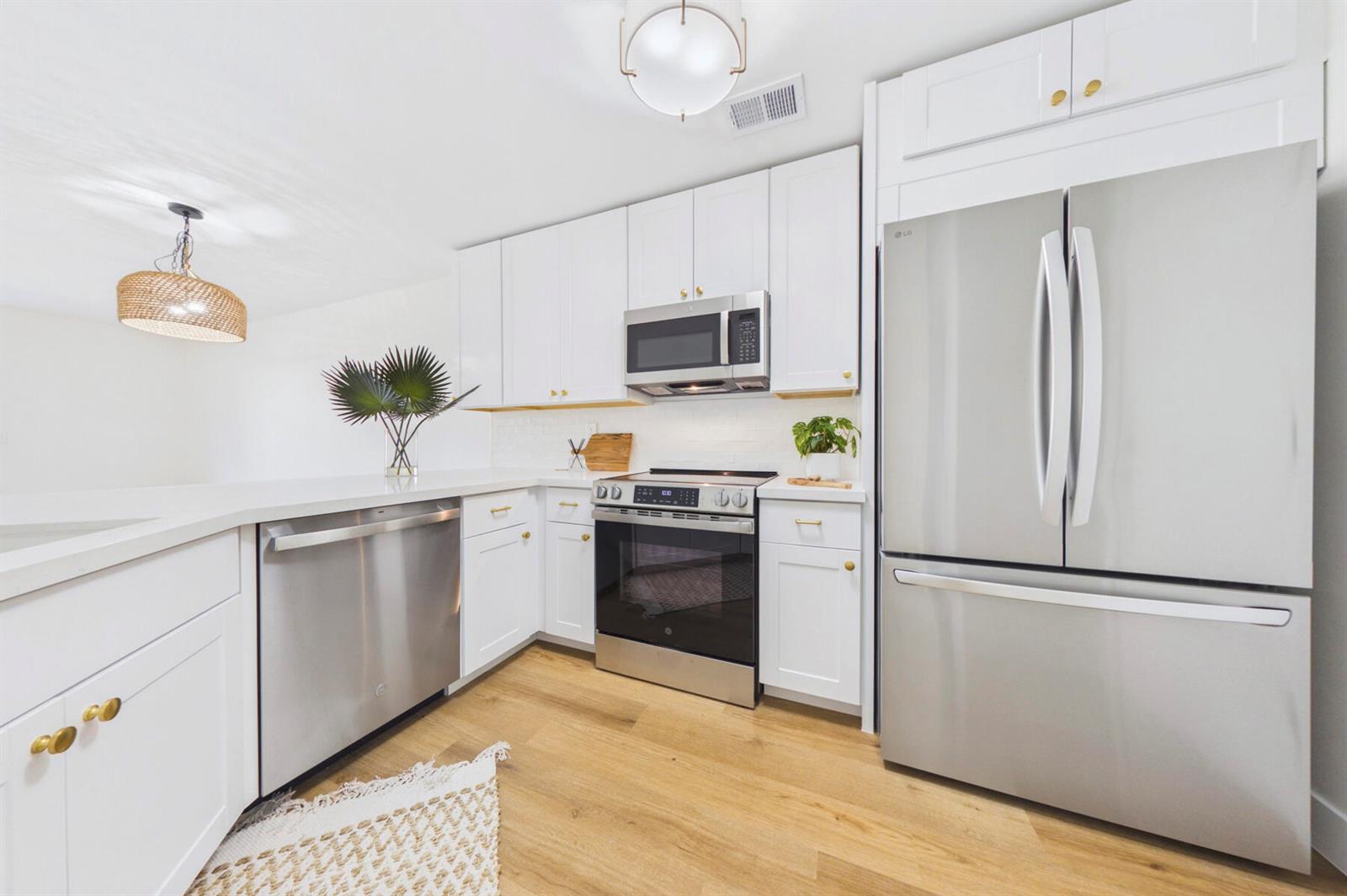 A modern kitchen features white cabinets, stainless steel appliances, and light wood flooring — 262 Timberwalk Trail, Jupiter FL 33458, JUPITER, FL