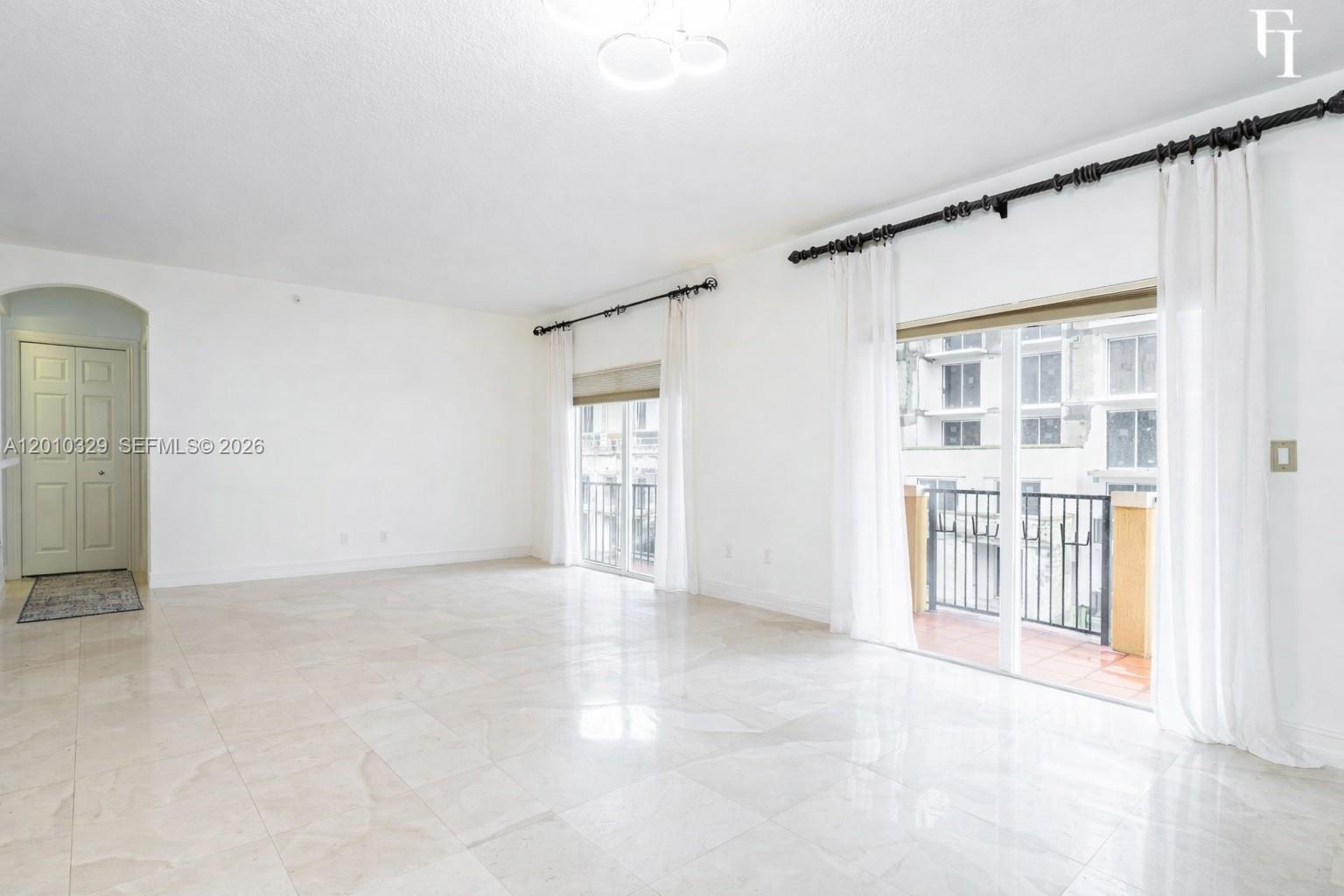 A bright, empty living room features white walls, polished tile floors, and two balcony access points — 322 Madeira Ave # 405, Coral Gables FL 33134, CORAL GABLES, FL