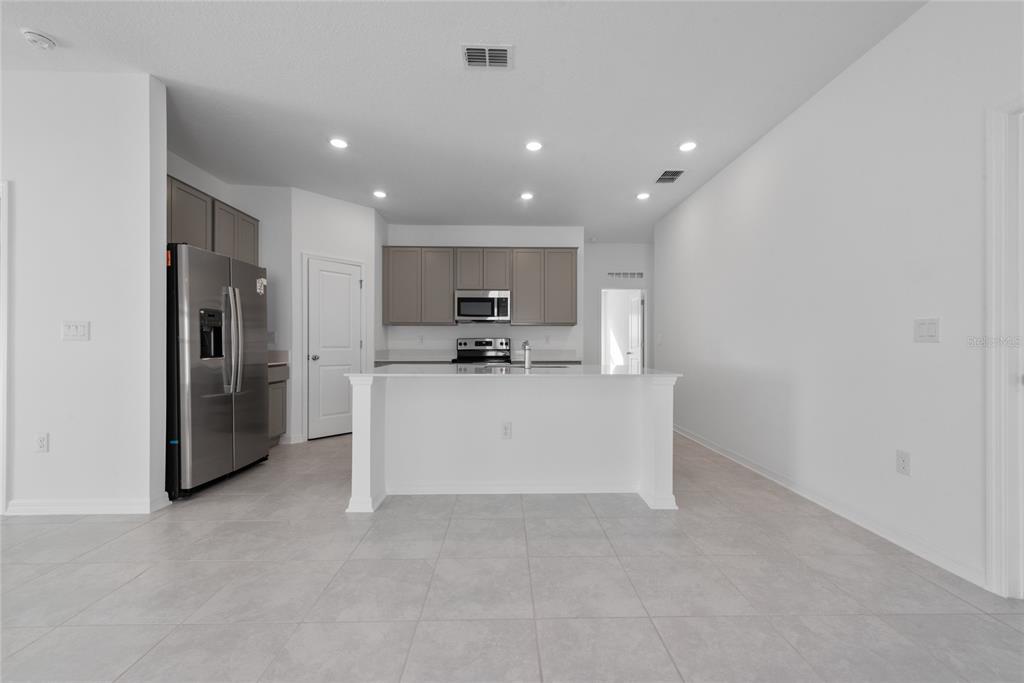 A kitchen features gray cabinets, stainless steel appliances, and white countertops on a tiled floor — 346 RUSTIC RAIL DRIVE, LAKE WALES, FL