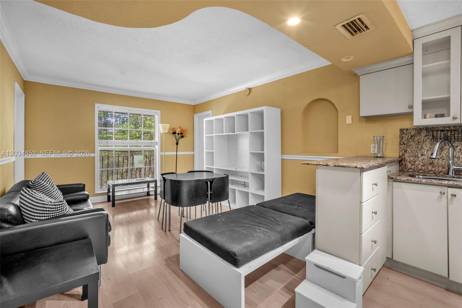 This living area features a kitchen counter, dining table, black sofa, and white shelving unit — 3245 Virginia St # 65, Miami FL 33133, MIAMI, FL