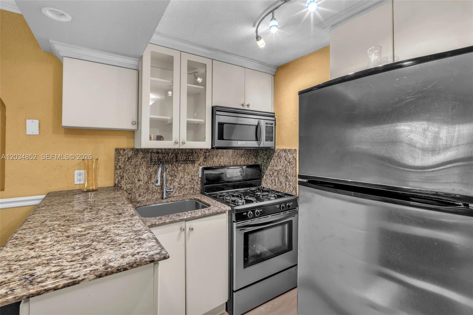 A kitchen features granite countertops, stainless steel appliances, and light-colored cabinetry against yellow walls — 3245 Virginia St # 65, Miami FL 33133, MIAMI, FL