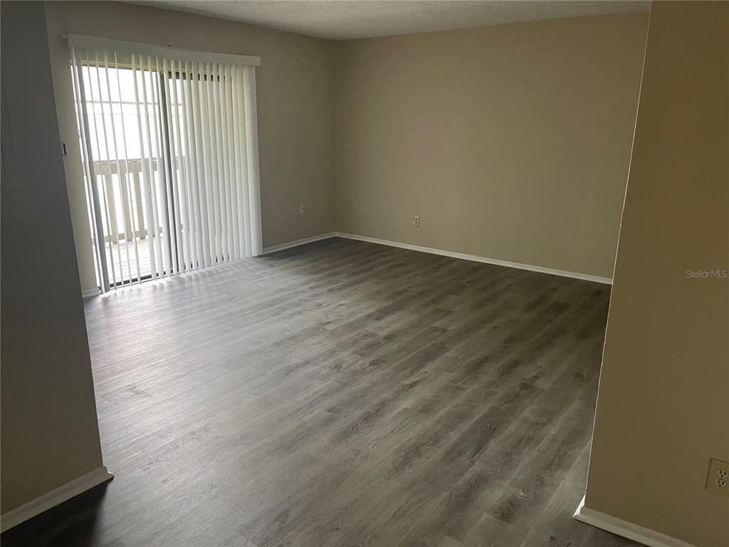 An empty living room features gray wood-look flooring, beige walls, and a sliding glass door — 137 SPRINGWOOD CIRCLE UNIT D, LONGWOOD, FL