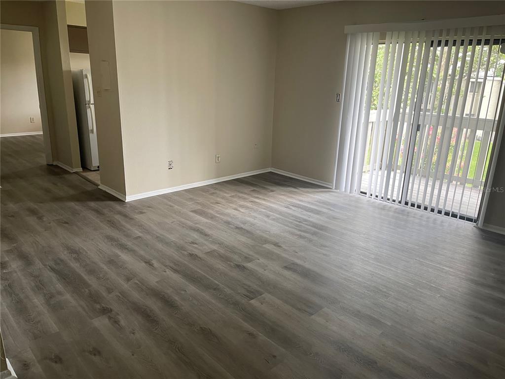 An empty living room features gray wood-look flooring, beige walls, and a sliding glass door — 137 SPRINGWOOD CIRCLE UNIT D, LONGWOOD, FL