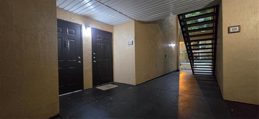 An outdoor apartment building walkway with two dark doors and a metal staircase — 7606 PISSARRO DRIVE UNIT 14106, ORLANDO, FL