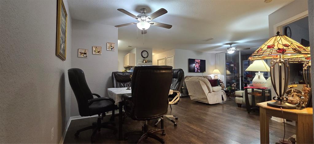 An open-concept living and dining area features dark wood flooring, ceiling fans, and neutral walls — 7606 PISSARRO DRIVE UNIT 14106, ORLANDO, FL