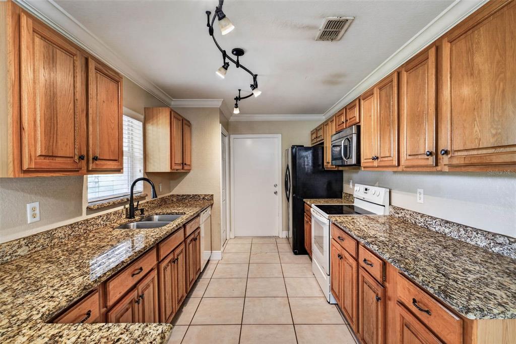 A galley kitchen features oak cabinets, granite countertops, tile flooring, and black and white appliances — 2820 LIVINGSTON ROAD, AVON PARK, FL