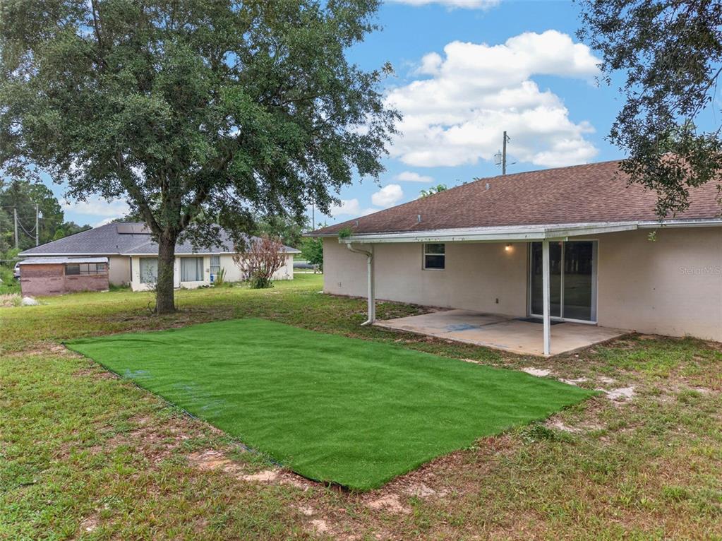A backyard features a concrete patio, a rectangular patch of artificial turf, and mature trees — 2820 LIVINGSTON ROAD, AVON PARK, FL