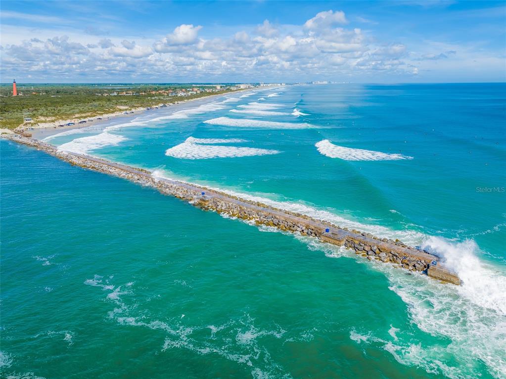 An aerial view of a stone jetty extending into the ocean near a sandy beach — 4863 S ATLANTIC AVENUE, PONCE INLET, FL