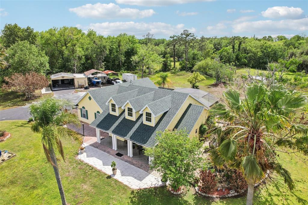 An aerial view of a yellow house with a green roof, dormers, and a patio — 3954 MCCLELLAND ROAD, ST CLOUD, FL