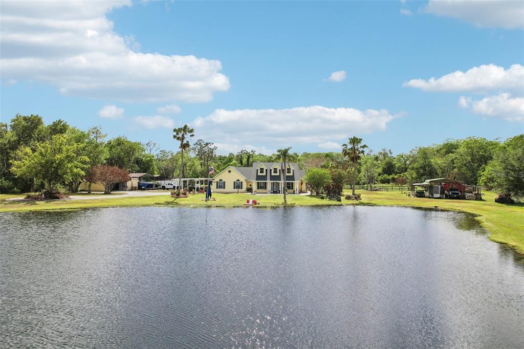 A yellow house with a pond in the foreground and trees in the background — 3954 MCCLELLAND ROAD, ST CLOUD, FL