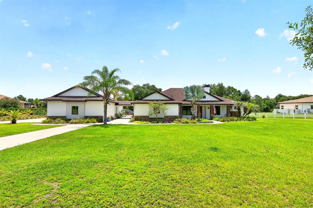 A single-story house with a white exterior, stone accents, and a large front lawn — 27324 GRAND OAK LANE, TAVARES, FL