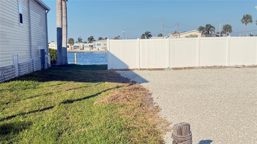 A gravel driveway sits beside a house and a white privacy fence near the water — 2858 TRINIDAD WAY, PALMETTO, FL