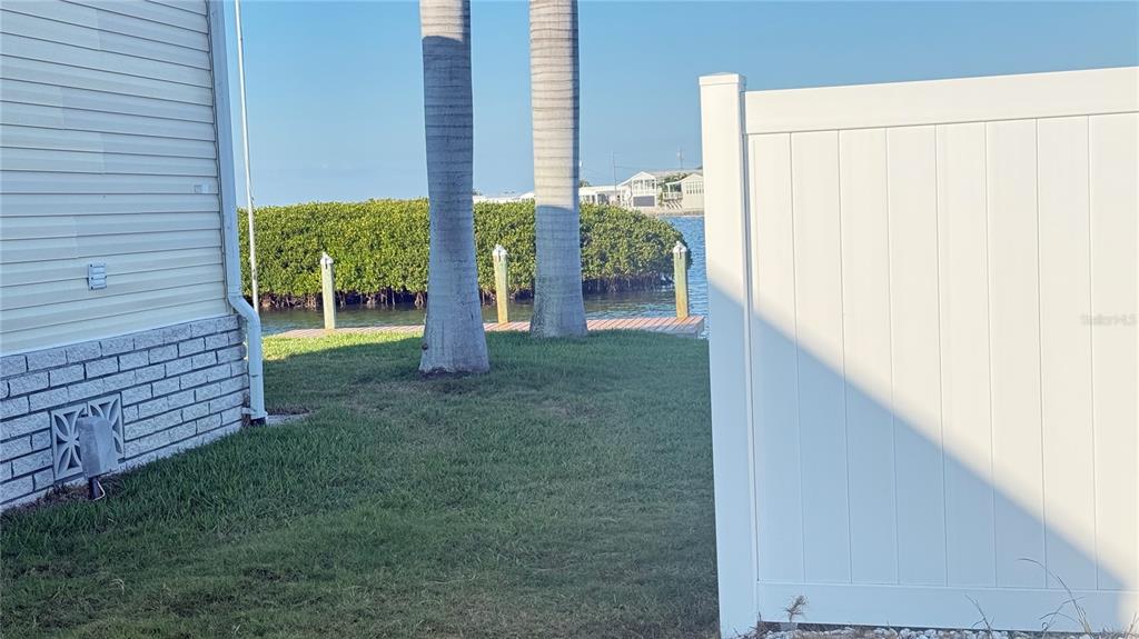 A view of a grassy yard with palm trees, a wooden dock, and a white fence — 2858 TRINIDAD WAY, PALMETTO, FL
