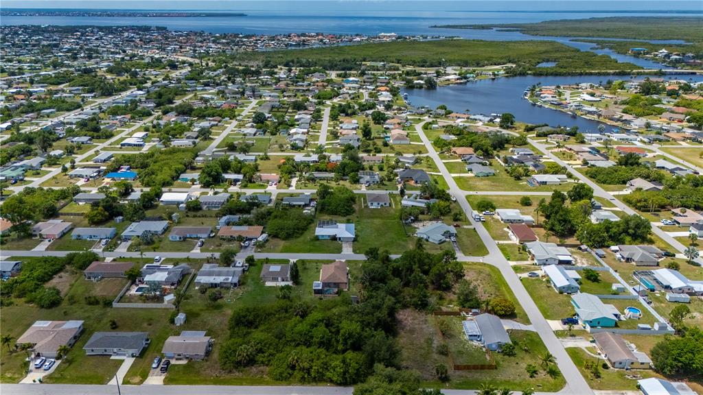 An aerial view shows a residential neighborhood with houses, green spaces, and a nearby waterway — 209 FORREST AVENUE NW, PORT CHARLOTTE, FL