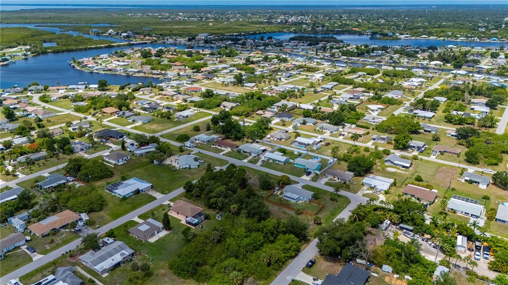 An aerial view shows a residential neighborhood with houses, green lawns, and nearby waterways — 209 FORREST AVENUE NW, PORT CHARLOTTE, FL