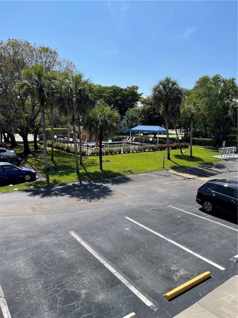 An outdoor view of a parking lot, green lawn, palm trees, and a swimming pool — 197 Lakeview Drive # 202, Weston FL 33326, WESTON, FL
