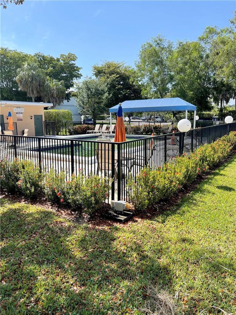 A fenced outdoor swimming pool area features a blue canopy, lounge chairs, and landscaping — 197 Lakeview Drive # 202, Weston FL 33326, WESTON, FL