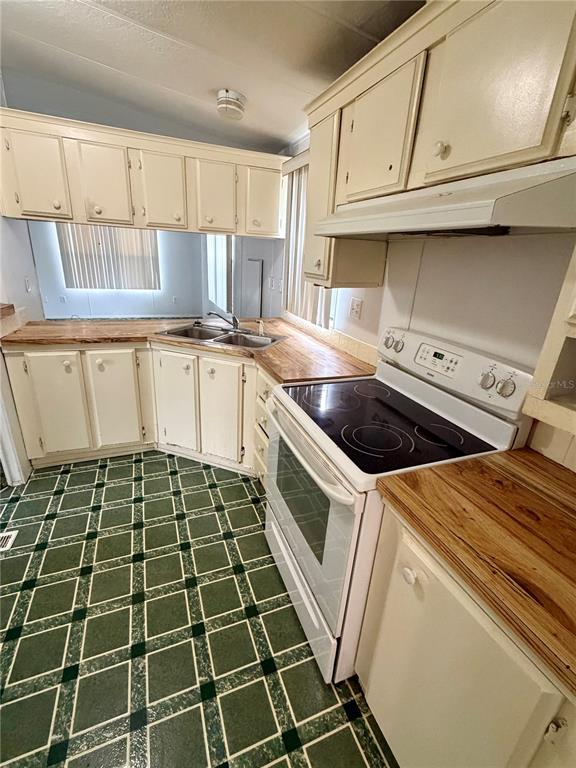 A kitchen features white cabinets, wood countertops, a white electric stove, and green tiled flooring — 820 WATER OAKS DRIVE, WINTER HAVEN, FL